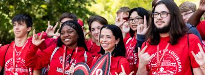 Students attending Orientation pose in matching red t-shirts, holding a fleur de lis sign